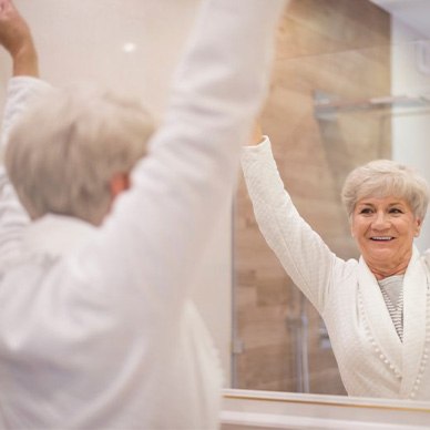 Woman raises her arms and smiling in the bathroom mirror