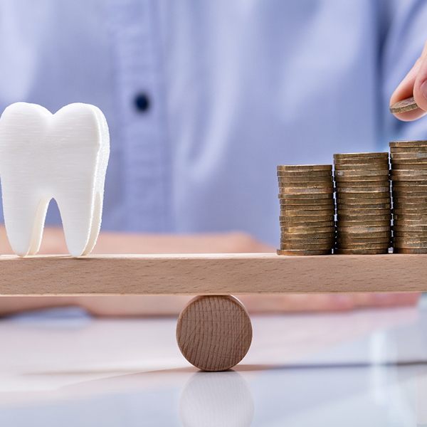 Tooth and stack of coins on wooden balance