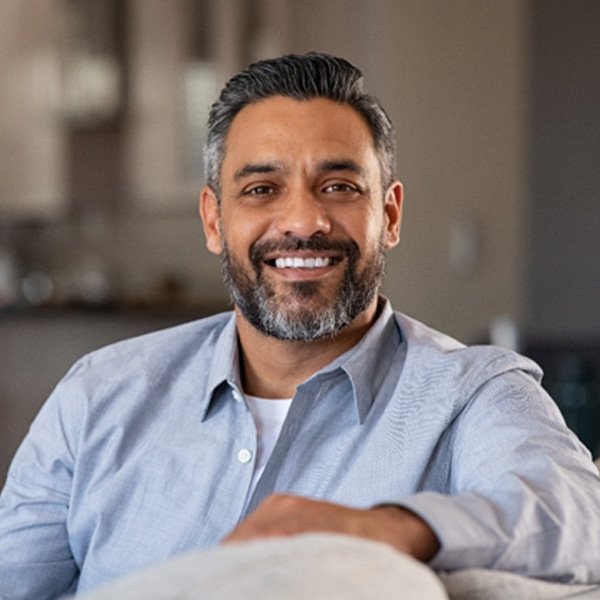 Smiling man with dental crowns in Hingham, MA leaning on couch