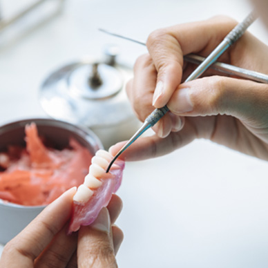 A lab worker adjusting a denture’s artificial teeth