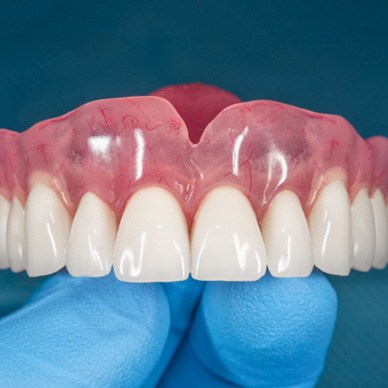 Close-up of gloved hand holding full dentures in Hingham, MA 