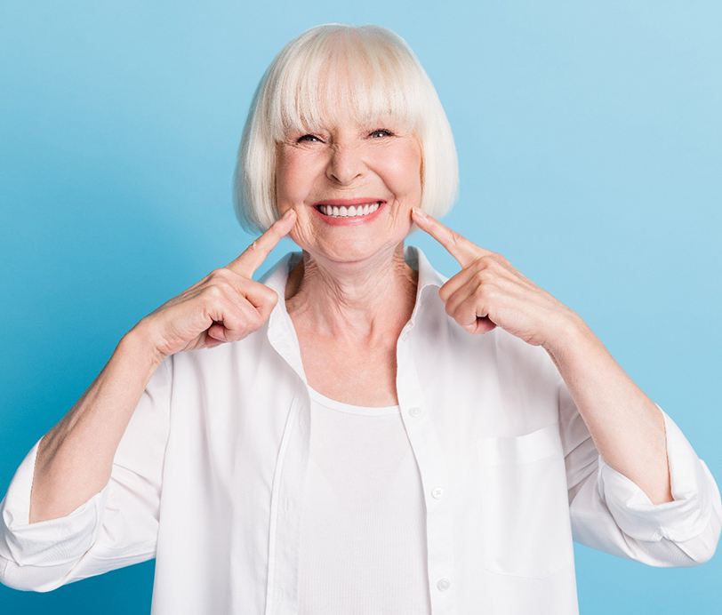 Woman pointing at her dentures in Hingham and smiling