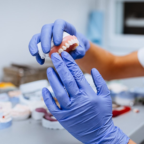 Gloved hands holding denture in laboratory setting