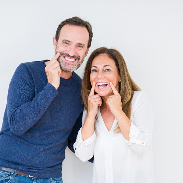 man and woman with dental implants in Hingham pointing to their smiles 