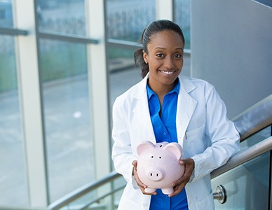 Dentist holding piggy bank representing the cost of dental implants in Hingham