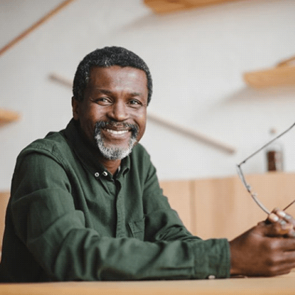 smiling man holding his glasses in front of him on table