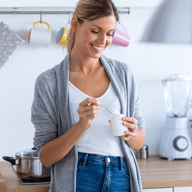 woman standing in her kitchen eating yogurt