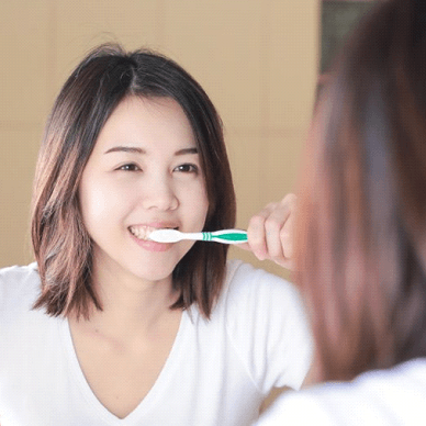 woman brushing her teeth in front of a mirror