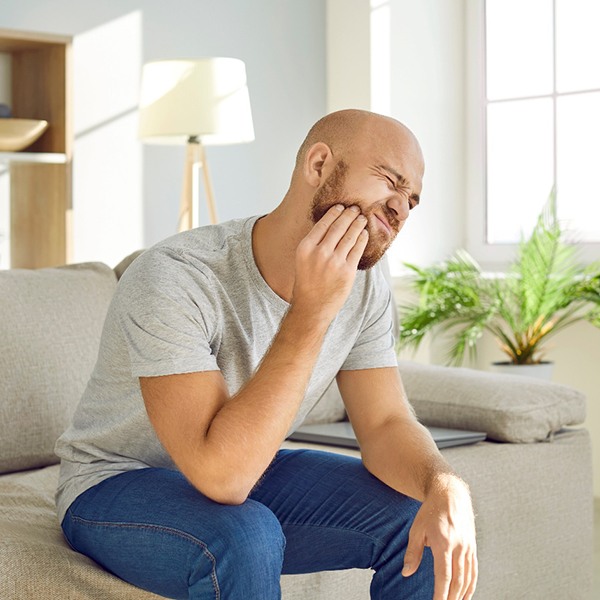 Bearded man on couch rubbing jaw in pain