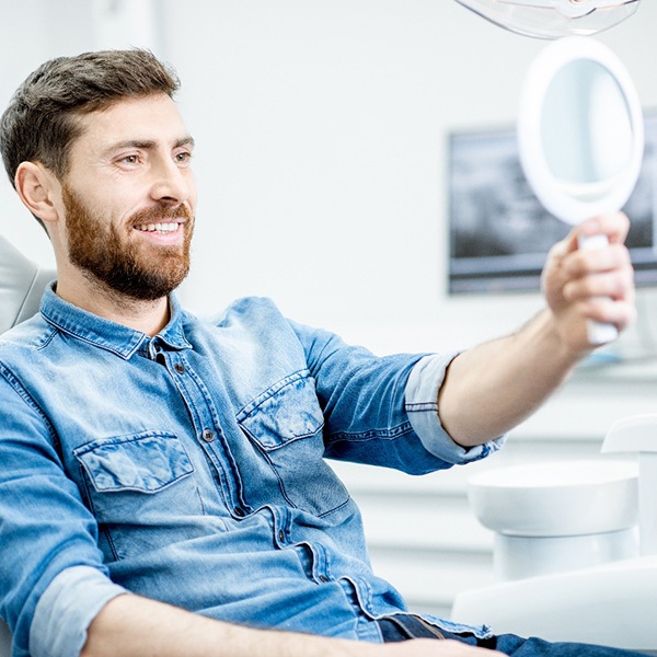 Smiling man looking in a handheld mirror at the dentist’s office