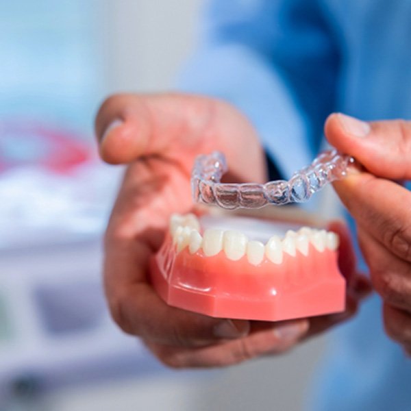 Dentist placing clear aligner on model of teeth