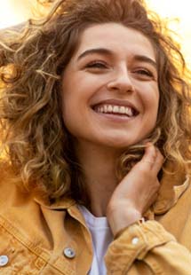 A smiling woman in an orange jacket after preventive dentistry visit near Weymouth