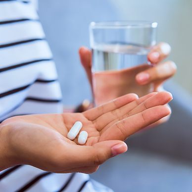 Someone in striped shirt holding 2 pills in one hand and glass of water in the other