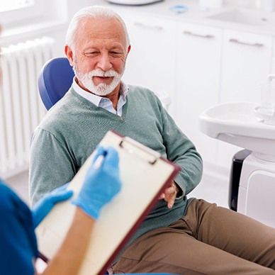 Dentist updating man’s medical history chart on clipboard