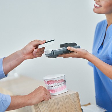 Patient holding card out to scanner for payment at desk with large model teeth