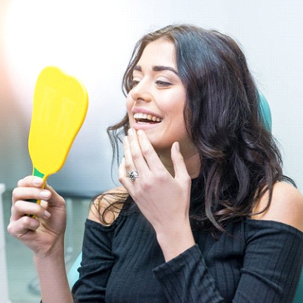 woman admiring her smile in a mirror after teeth whitening