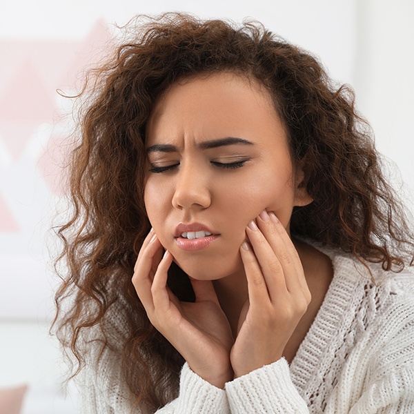 Young woman holding jaw in pain before wisdom tooth extractions